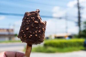 Bitten chocolate popsicle ice cream bar with crushed peanut nuts photo