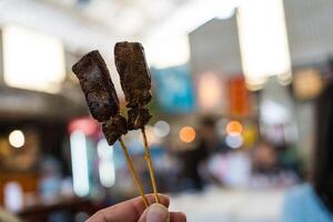 Hand holding bamboo skewers with liver pork satay. photo