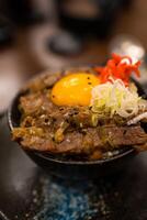 Roast Wagyu beef rice and raw egg bowl in a black bowl. photo