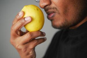A Man Holding a Bright Yellow Lemon Close to His Face, Engaging with Its Aromatic Essence photo