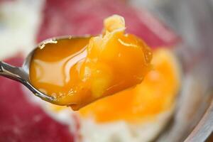 CloseUp of a Spoon with a Runny Egg Yolk on Fried Egg Whites, a tasty and healthy breakfast photo