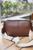 A Stylish Brown Leather Bag with a Strap Placed on a Rustic Wooden Table Surface photo