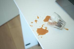 A drink was accidentally spilled on a desk with a laptop and glasses, creating a mess photo