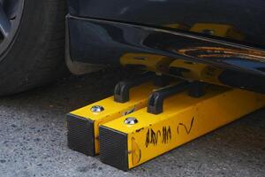 The Vehicle Wheel Lock is currently applied to the Black Car parked on the street photo