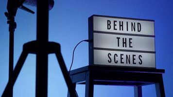 Behind the scene light box in front of vdo camera frame. Black text on white lightbox of word Behind the scenes. Prop for filmmaker movie or film studio. Footage for B roll film production making of. video