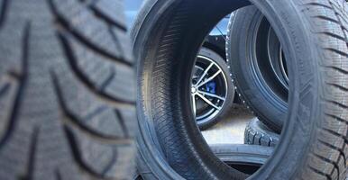 Car is visible through the new tires staying on the edge. Stacked tires set ready to be mounting on a car photo