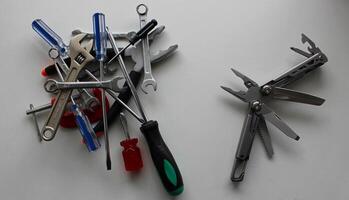 Multitool and a stack of variety hand tools on different sides of a white table photo