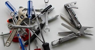 Half-opened full metal multi-tool with different blades and stacked multi-colored tools on a white table photo