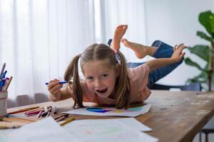 With smile 5-year-old girl giggles while creating art at the table with vibrant colored pencils photo