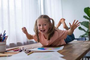 A 5-year-old girl laughs joyfully as she draws at the table, surrounded by colorful pencils photo