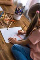 A 5-year-old girl happily draws at a table surrounded by a rainbow of colorful pencils,top view photo