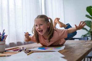 A 5-year-old girl laughs joyfully as she draws at the table, surrounded by colorful pencils photo