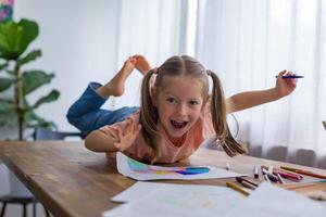 Laughing and having fun,5-year-old girl creates her artwork at the table filled with bright pencils photo