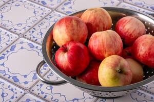 Red apples lie in a metal colander on a table with a blue and white tile surface photo