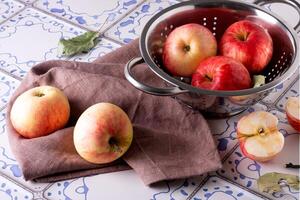 Red apples lie on a linen napkin and in a colander on a table photo