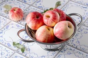 Red apples lie in a metal colander on a table with a blue and white tile surface photo