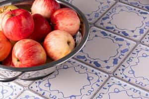 Red apples lie in a metal colander on a table with a blue and white tile surface photo