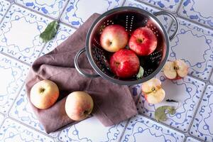 Red apples lie on a linen napkin and in a colander on a table photo
