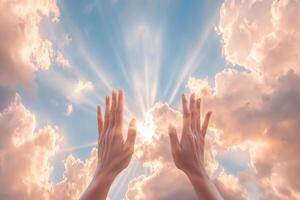 Two hands reaching toward a glowing sky with rays of sunlight breaking through clouds photo