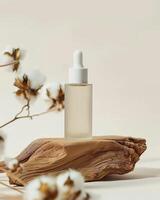 A bottle of oil sits on a wooden block with cotton flowers photo