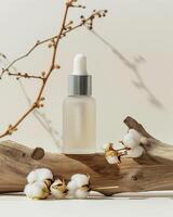 A bottle of cosmetic oil sits on a branch with cotton flowers photo