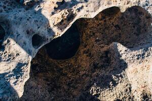 a textured landscape of wet, rocky terrain with shallow pools of water, surface appears rugged and uneven, showcasing natural erosion patterns photo