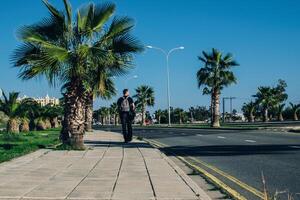 man walks along a road with palm trees on the side photo
