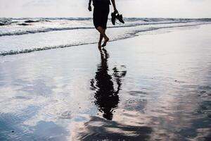 a man walks along the beach, reflection in the wet sand photo