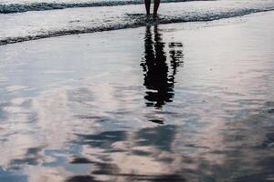 a man walks along the beach, reflection in the wet sand photo