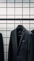 Black suit jacket hanging on rack against tiled wall photo