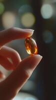 Close-up of a hand holding an amber capsule against a blurred background. Health and wellness concept photo