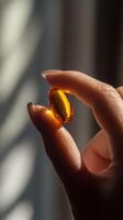 Close-up of hand holding orange capsule, sunlight reflection. Health and wellness concept photo