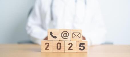 Contact Us concepts. Happy New Year 2025 with Wood block of Email, call Phone and Website Address sign against Doctor background. Healthcare Customer support hotline, health and communication concept photo