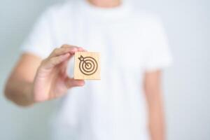hand hold dartboard block with business goal, strategy, target, mission, action, objective, aim and success concept photo
