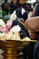 Hand of people picks up the paper flower from the tray during funeral in Buddhism temple with blurred crowded people in background photo