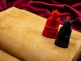 yellowed medieval ancient blank book open on a table with small statues representing figures of the King and Queen. photo