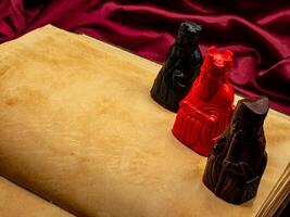 yellowed medieval ancient blank book open on a table with small statues representing figures of the King, the bishop and Quee photo