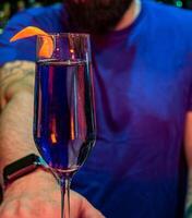 close-up shot of a glass with a purple colored alcoholic drink and pink flowers in the background on a bar counter photo