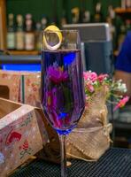 close-up shot of a glass with a purple colored alcoholic drink and pink flowers in the background on a bar counter photo