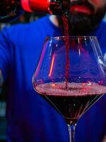 vertical close-up shot of a glass where the bartender pours red wine photo