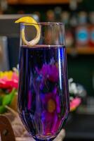 close-up shot of a glass with a purple colored alcoholic drink and pink flowers in the background on a bar counter photo