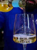 vertical close-up shot of a glass where the bartender pours white wine photo