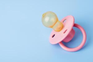 Pink baby pacifier on a blue background, space for text photo