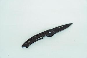 Mini size folding knife of solid black color partially opened isolated on white background. Close-up view of a black folding knife used for various outdoor or survival activities photo