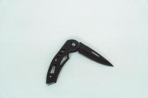 Mini size folding knife of solid black color partially opened isolated on white background. Close-up view of a black folding knife used for various outdoor or survival activities photo