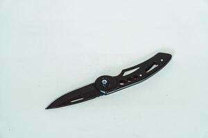 Mini size folding knife of solid black color partially opened isolated on white background. Close-up view of a black folding knife used for various outdoor or survival activities photo