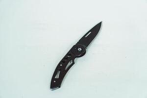 Mini size folding knife of solid black color partially opened isolated on white background. Close-up view of a black folding knife used for various outdoor or survival activities photo