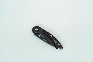 Mini size folding knife of solid black color partially opened isolated on white background. Close-up view of a black folding knife used for various outdoor or survival activities photo