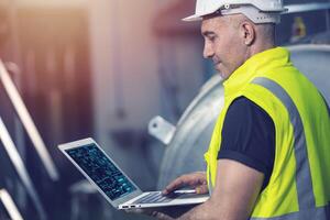 Smart Engineer using laptop computer software program application to help support work service machine on site factory. photo