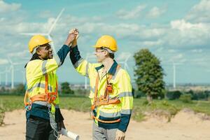 Engineer team stress hand together happy smiling greeting job done at Turbines field wind electricity power generator farm outdoor. photo